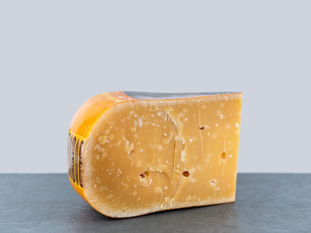 Slice of 3yrs Aged Vintage Gouda cheese with caramel notes and salt crystals, displayed against a grey background