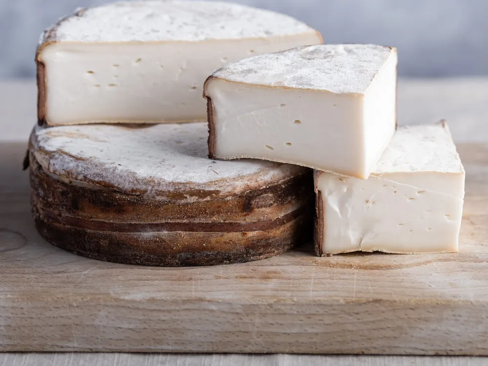 A Plancherin d'Arêches cheese wheel, wrapped in a band of sapwood and cut into triangular pieces, reveals its smooth, white interior, resting on a wooden surface