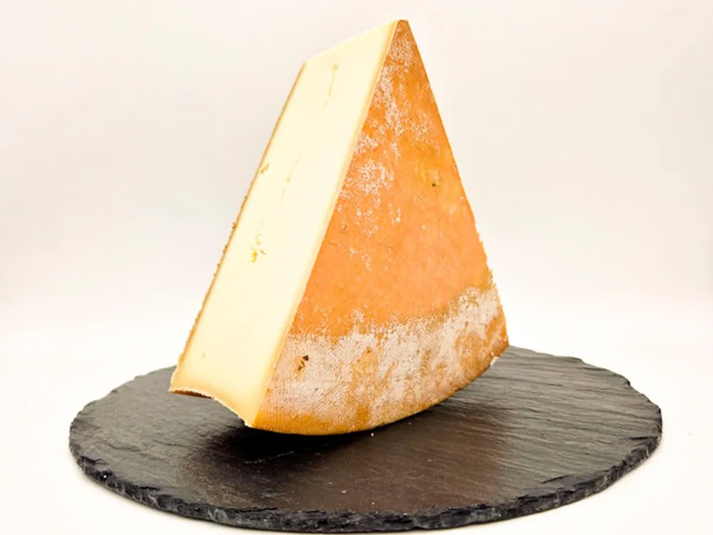 A triangular slice of Abondance cheese sits on a round marble surface, revealing its pale-yellow interior