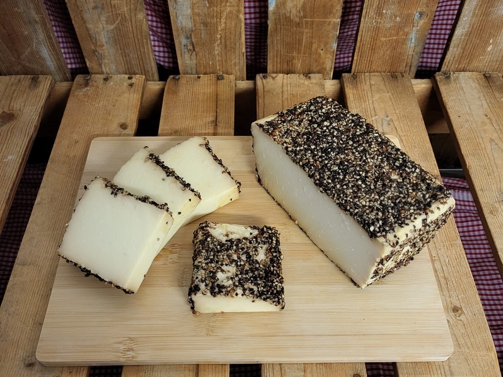 A block of Hotspur cheese, coated in cracked black pepper, is arranged on a wooden cutting board alongside several slices