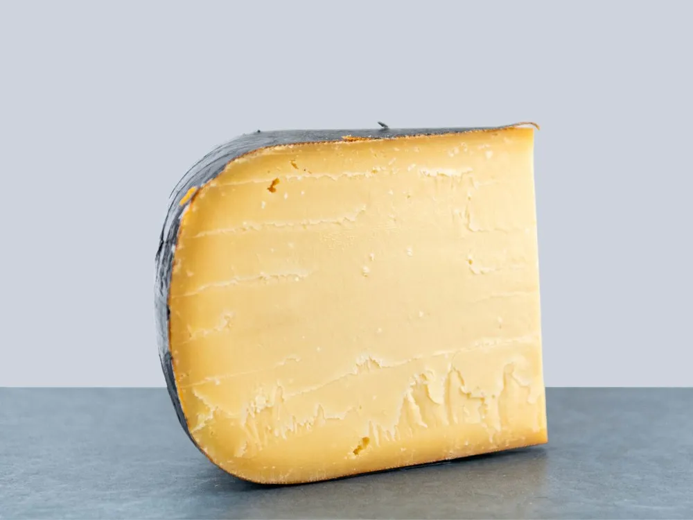 A wedge of Old Dutch Gouda cheese with a deep golden yellow color, displayed against a grey background