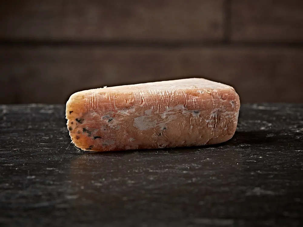 A wedge of Alex James Co. No. 5 Grunge cheese rests on a wooden surface