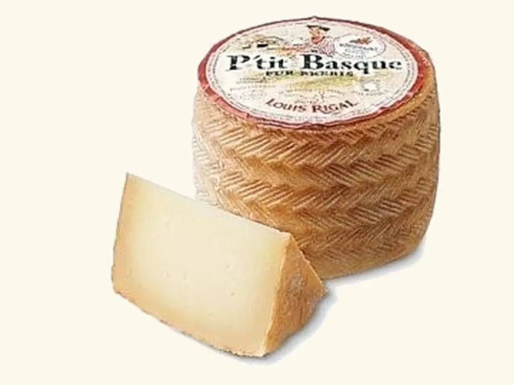 A cylindrical P'tit Basque cheese with a slice cut to showcase the distinctive basket-weave pattern on its rind