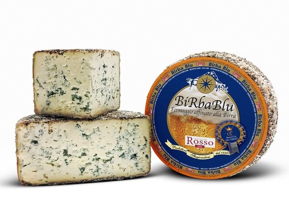 A wheel of Birba Blu cheese with its label, accompanied by a stacked half-cut and a slice, all set against a white background