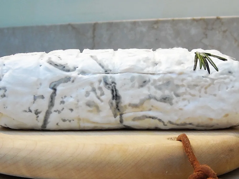 Bosworth cheese log showcasing white rind rests on a wooden board