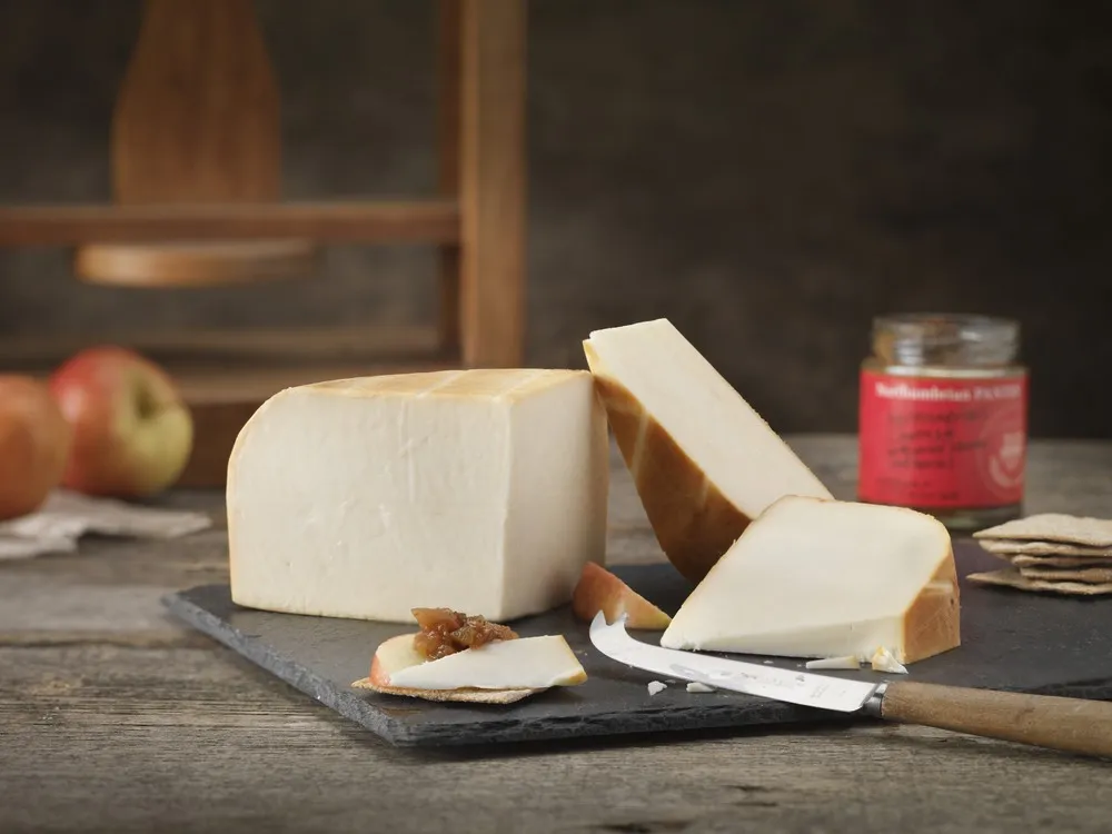 Large slices of Chesterwood cheese, apples, crackers and a knife, sits on a black marble slab, all arranged on a wooden surface