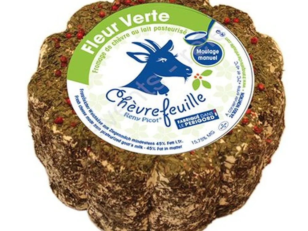 A labeled Chevrefeuille cheese, adorned with pink peppercorns and herbs, is set against a white background.