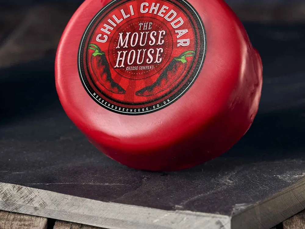 A wax-coated Mouse House Chili Cheddar cheese disc, featuring a label, resting on a black marble surface