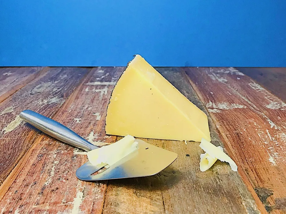 A slice of Cornish Kern cheese with a cheese slicer placed on a wooden surface