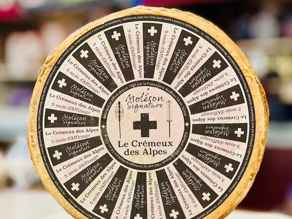 A wheel of Crémeux des Alpes Signature cheese featuring a label that provides detailed information about the cheese