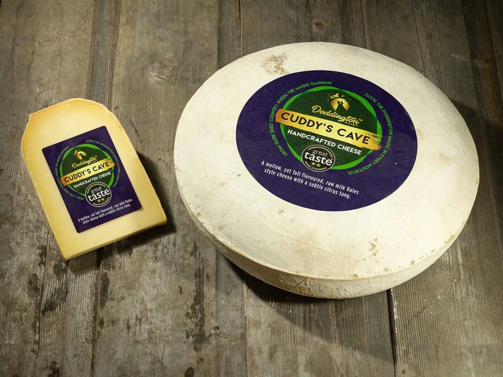 A wheel of Cuddy's Cave cheese, sits next to a slice of the cheese on a wooden surface