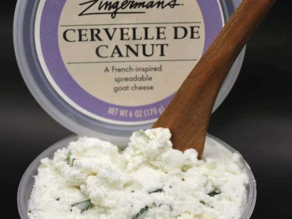 A container of Cervelle de Canut cheese with a lid displaying the cheese's details