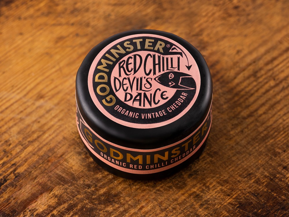 Godminster Red Chilli Devil's Dance Organic Vintage Cheddar enrobed in black wax to protect it, rests on wooden surface