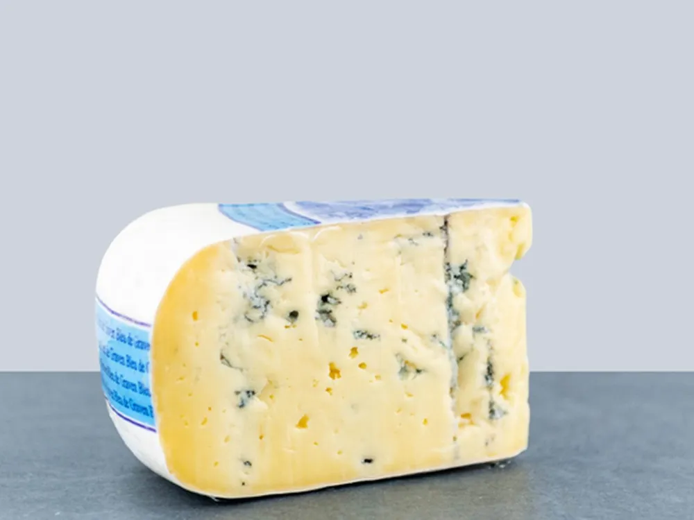 A slice of Dutch Blue cheese, showcasing blue veins and a creamy, smooth interior, rests on a grey surface