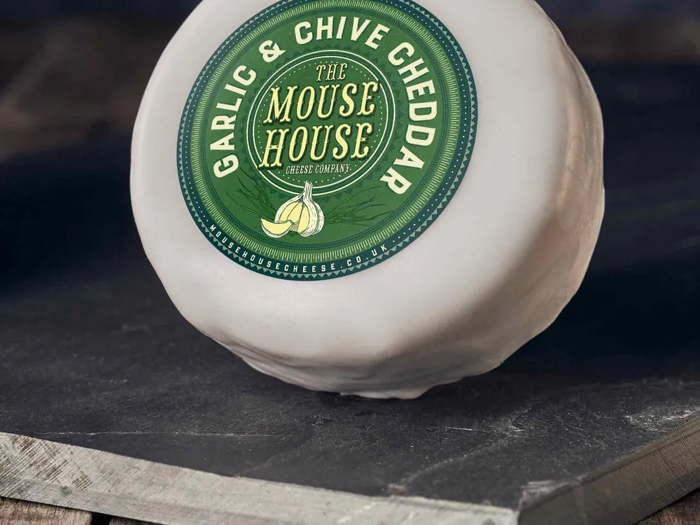 A wax-coated Mouse House Garlic & Chive Cheddar rests on a sleek black surface