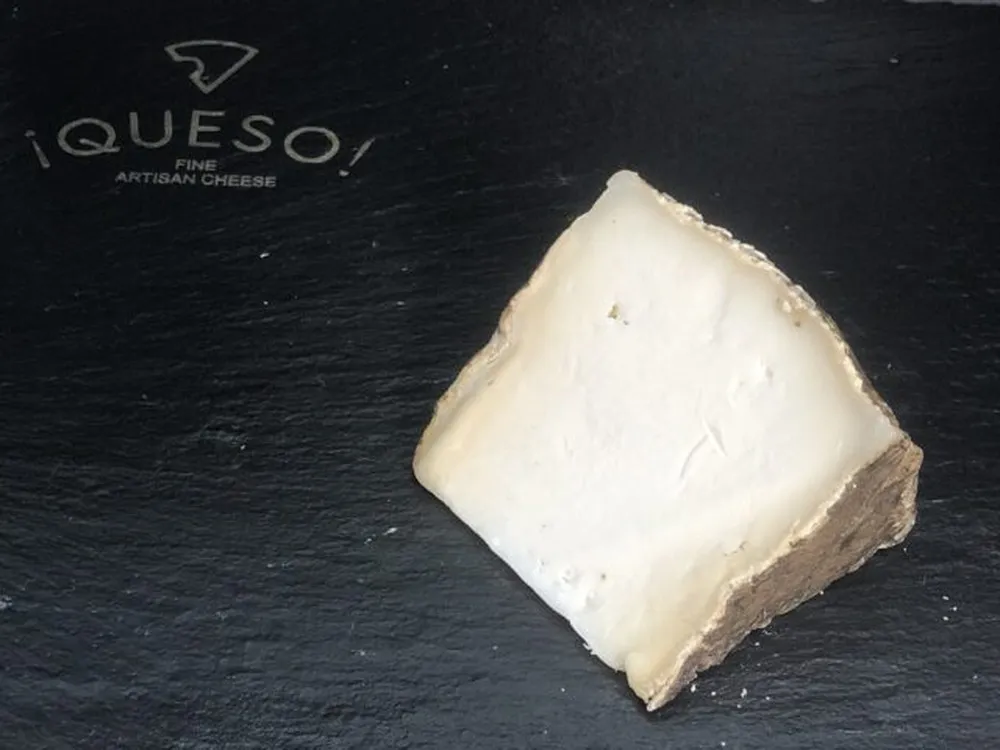 A slice of Garrotxa cheese, showcasing its ivory interior, rests on a black marble surface