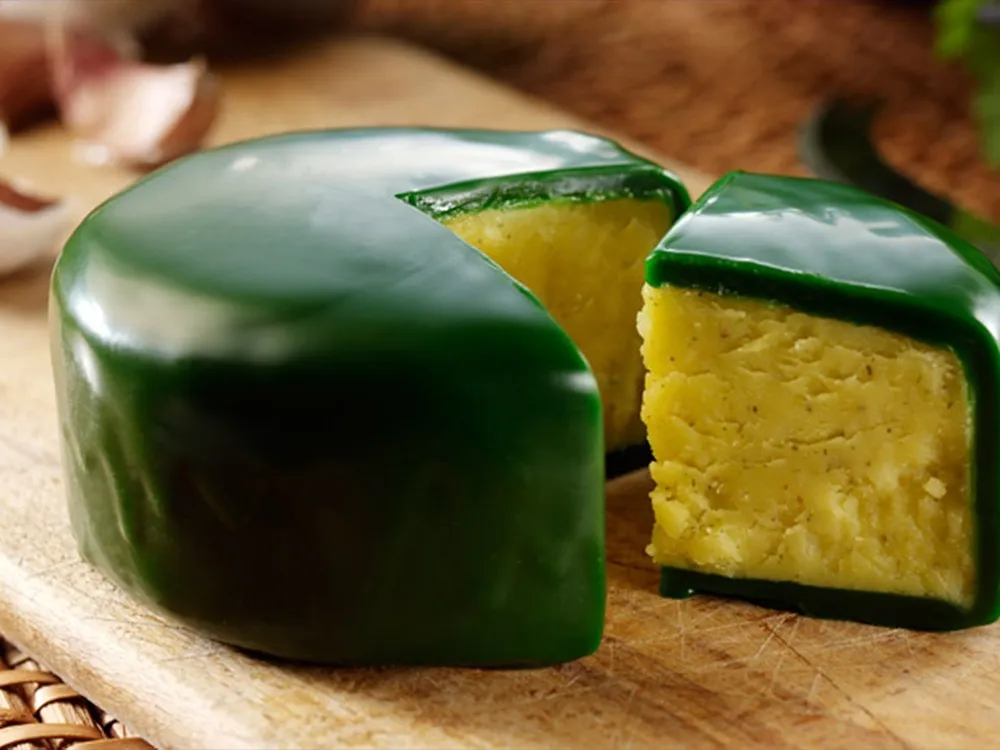 A partially cut truckle of Green Thunder cheese, encased in emerald-colored wax, rests on a wooden board