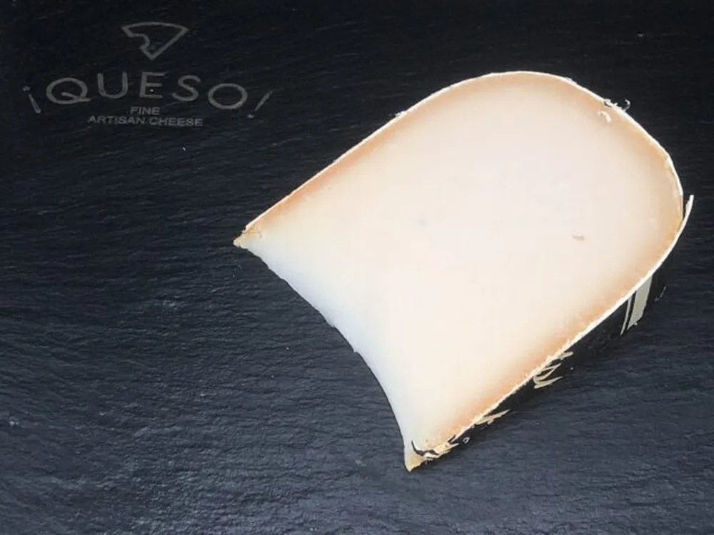 A wedge of Goat Gouda cheese sits on a black surface