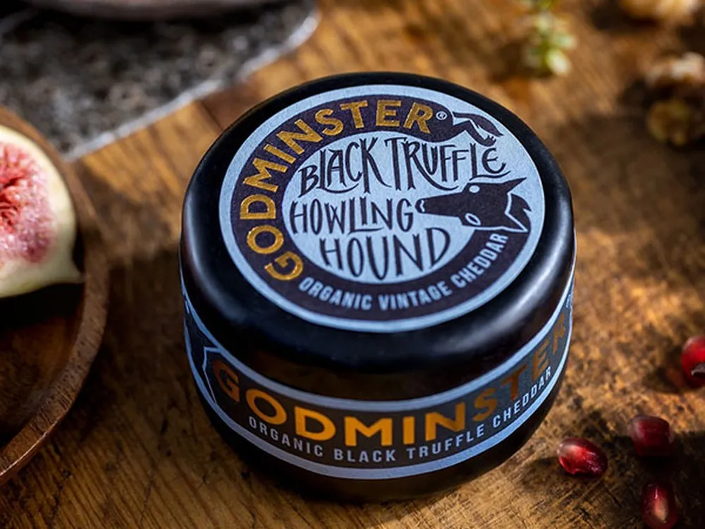 Godminster Black Truffle Howling Hound Organic Vintage Cheddar enrobed in black wax to protect it, rests on wooden surface