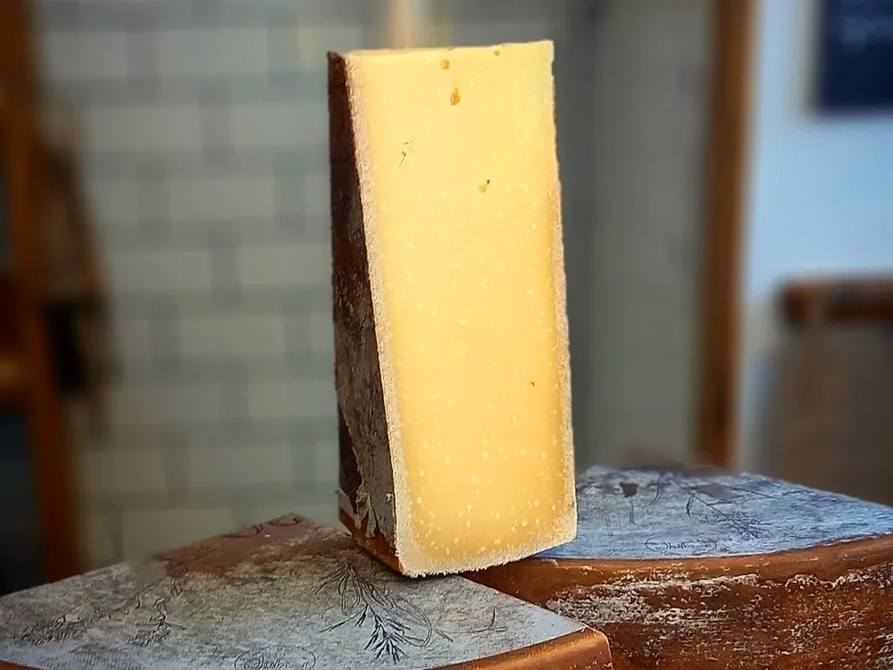 A slice of Alpkäse cheese resting on top of cut wheels of the same cheese, revealing its rich, golden-yellow interior