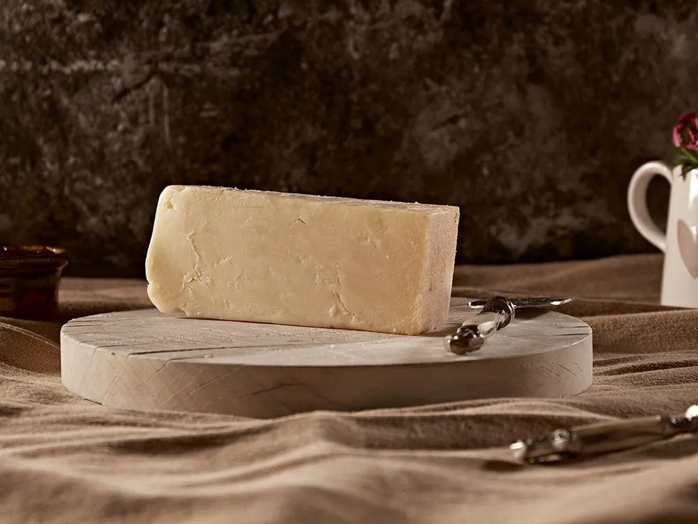 A wedge of Isle of Mull cheese sits on a round wooden cutting board, accompanied by a cheese knife