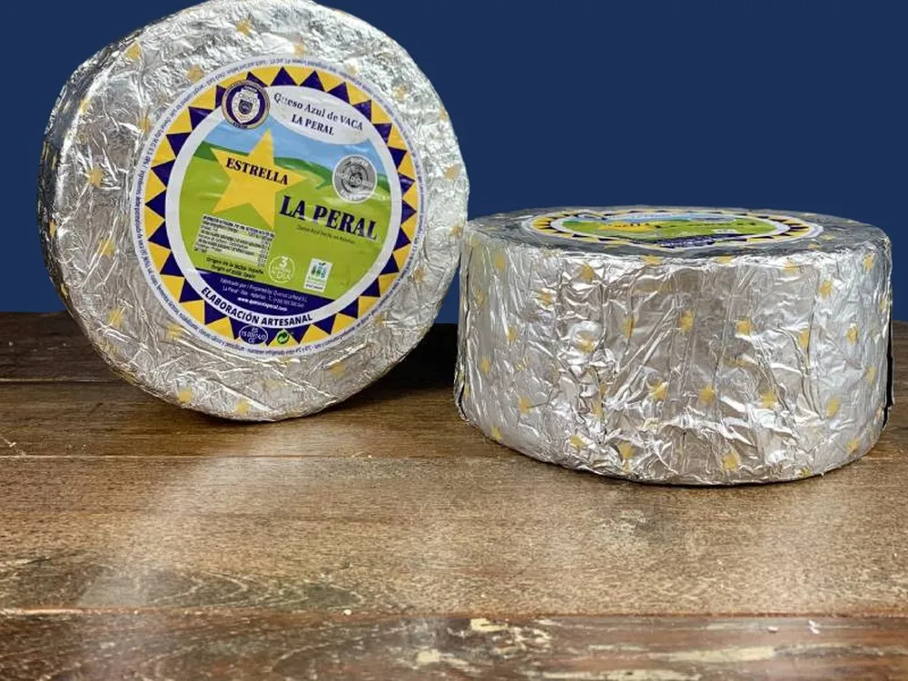 Discs of La Peral cheese, wrapped in silver paper with labels, are arranged on a wooden surface