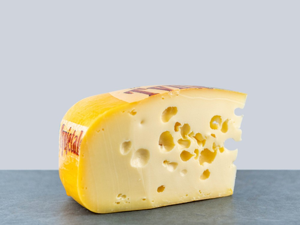 A slice of a Maasdam cheese with a dark rind, revealing smooth yellow interior with eyes (holes).