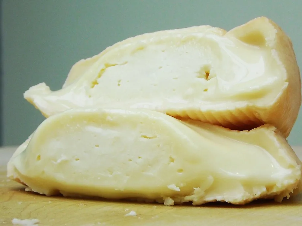 Munster cheese, revealing its soft interior and washed rind, resting on a wooden surface