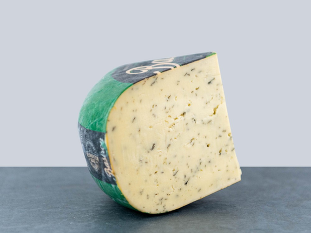 A wheel of Nettle cheese with a slice cut out displayed on a flat surface