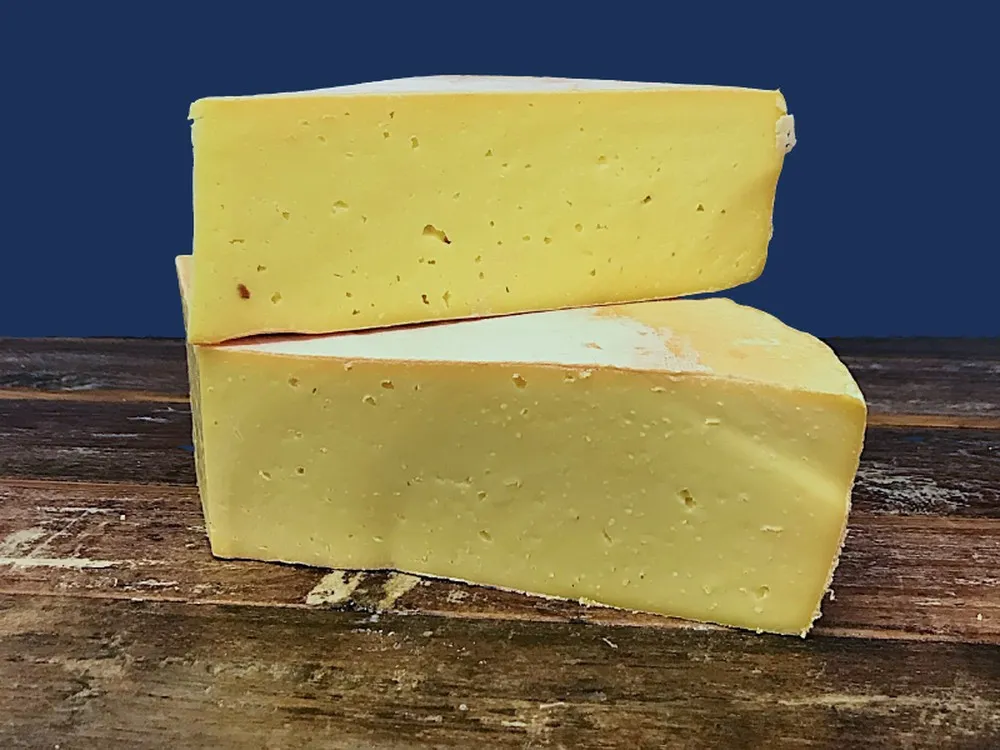 Wedges of Ogleshield cheese, revealing their creamy color, are stacked on a wooden surface