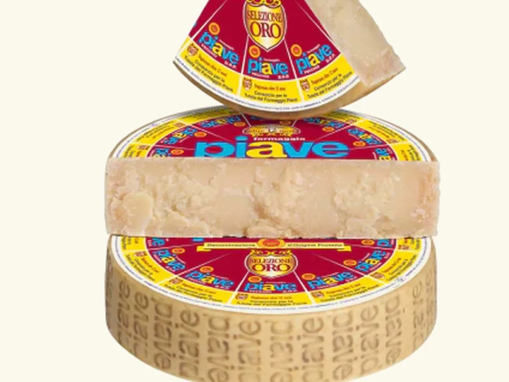 A wheel of Piave Vecchio cheese, wrapped and stacked, with a half-cut and triangular slice displayed against a white background