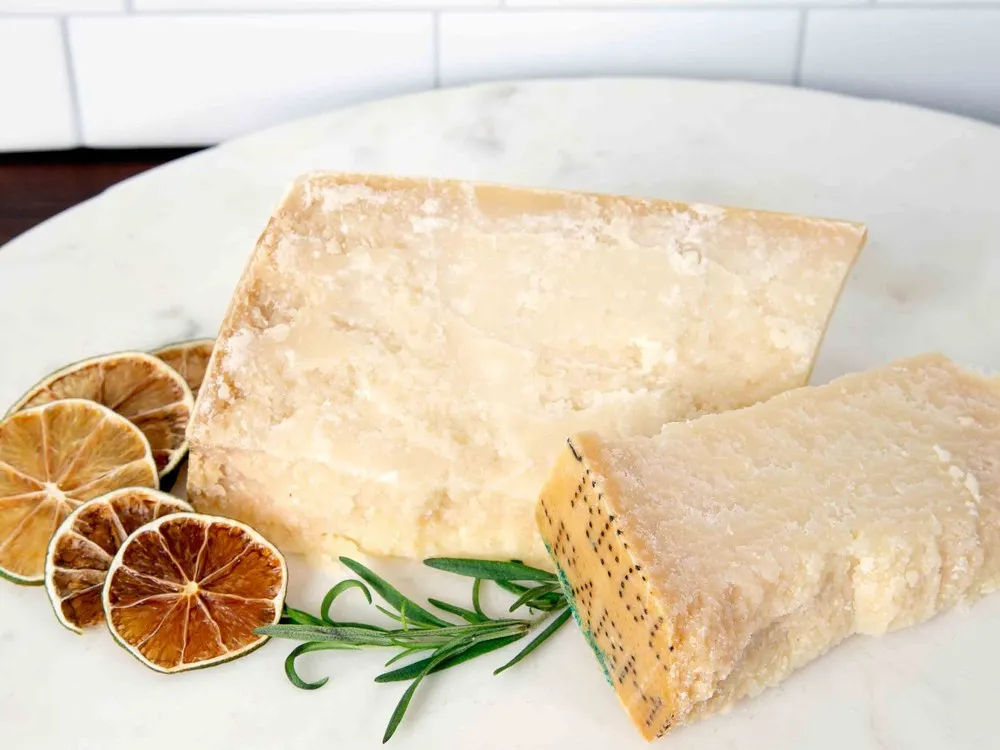 Slices of Cravero Parmigiano Reggiano arranged on a white plate, accompanied by dried lemon slices and fresh herbs