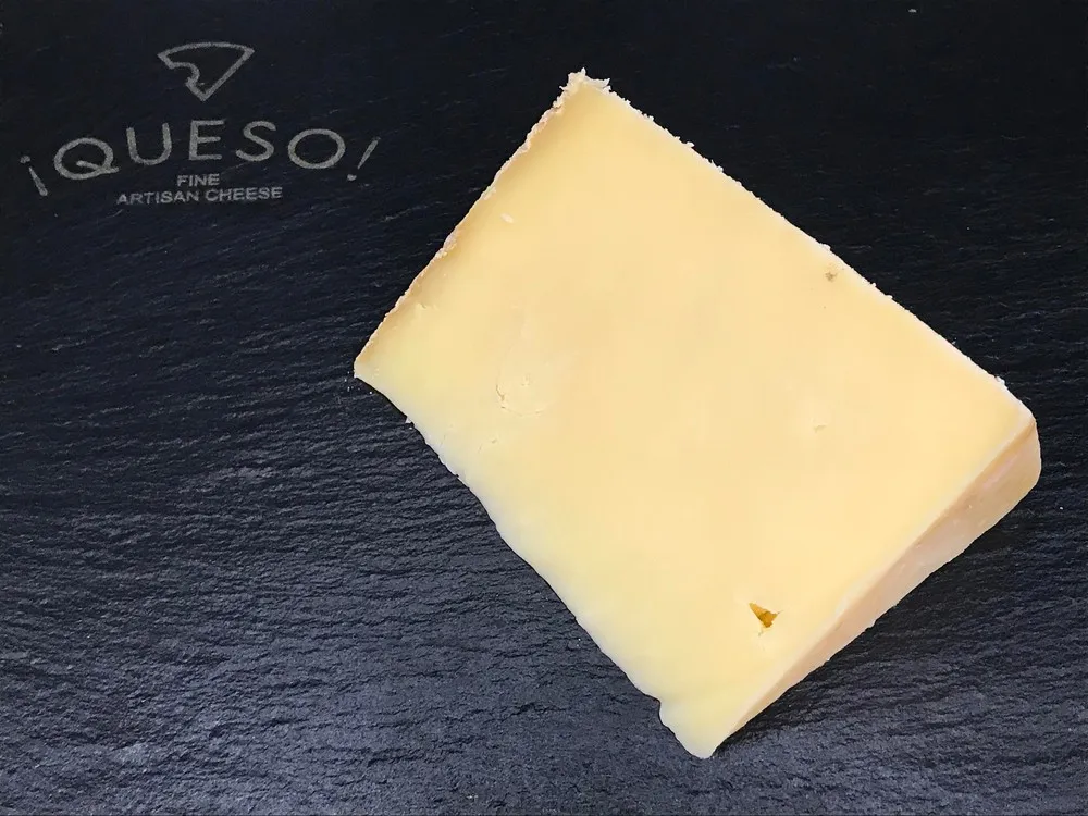 A slice of Pitchfork Cheddar cheese, featuring a pale yellow hue, displayed on a black marble surface