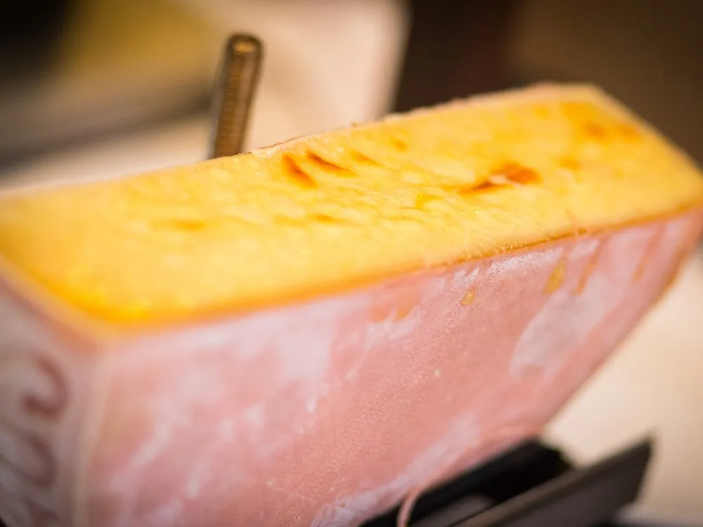 A partially sliced Raclette cheese revealing its soft interior, paired with a cheese cutting tool