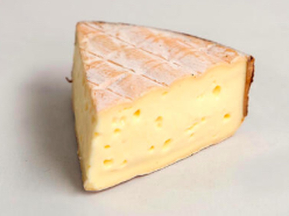 A slice of Rollright cheese, showcasing its peachy-pink rind and spoonable, silky paste.