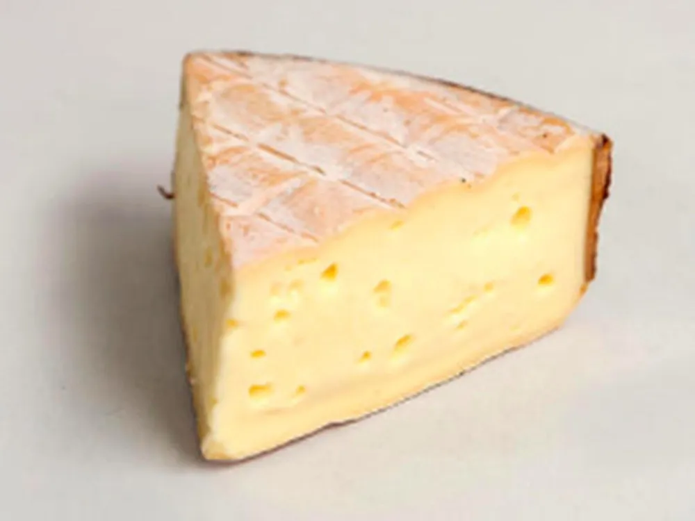 A slice of Rollright cheese, showcasing its peachy-pink rind and spoonable, silky paste.