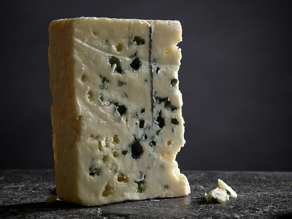 A slice of Roquefort cheese, revealing its smooth, creamy interior with blue veins, placed on a black surface