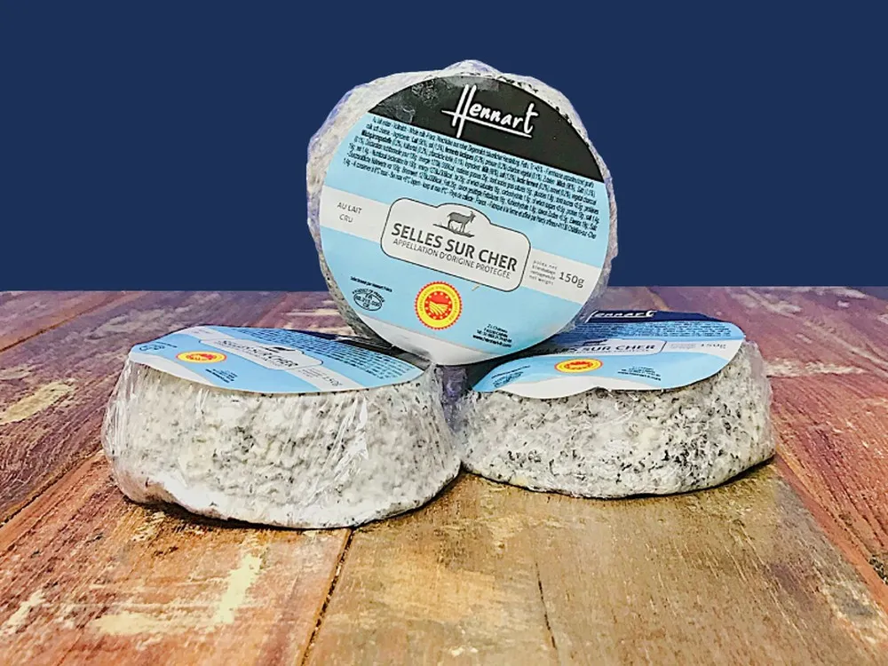 Plastic-wrapped discs of Selles-sur-Cher cheese, with labels, neatly arranged on a wooden surface