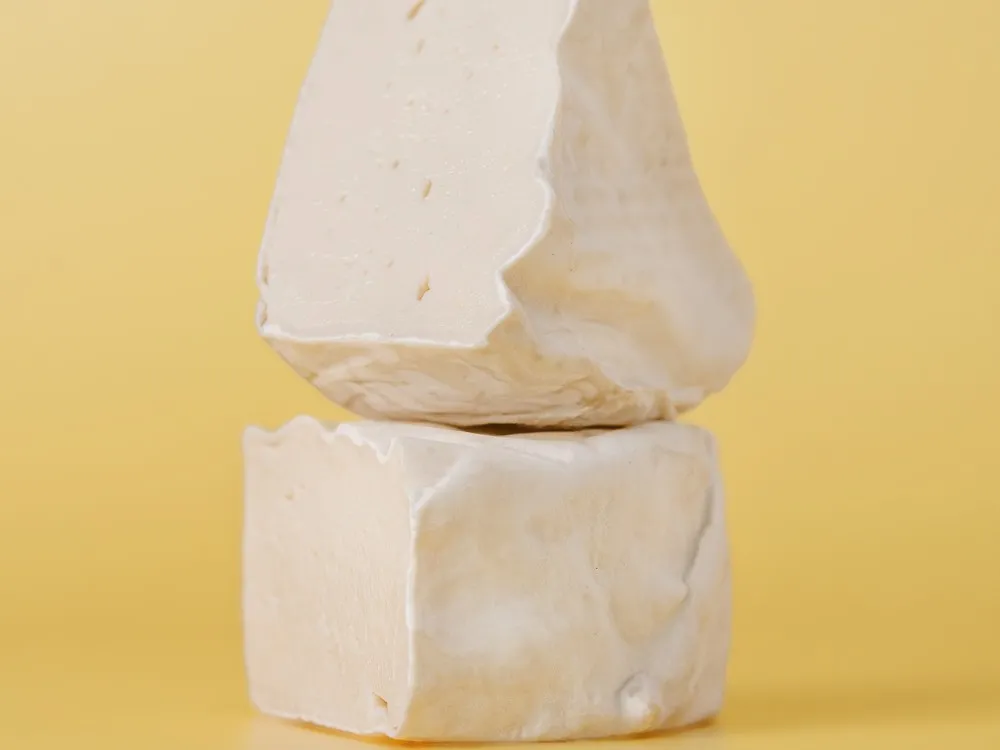 Pieces of Shamembert, a vegan cheese, showing creamy interior and natural rind, are arranged against a yellow background