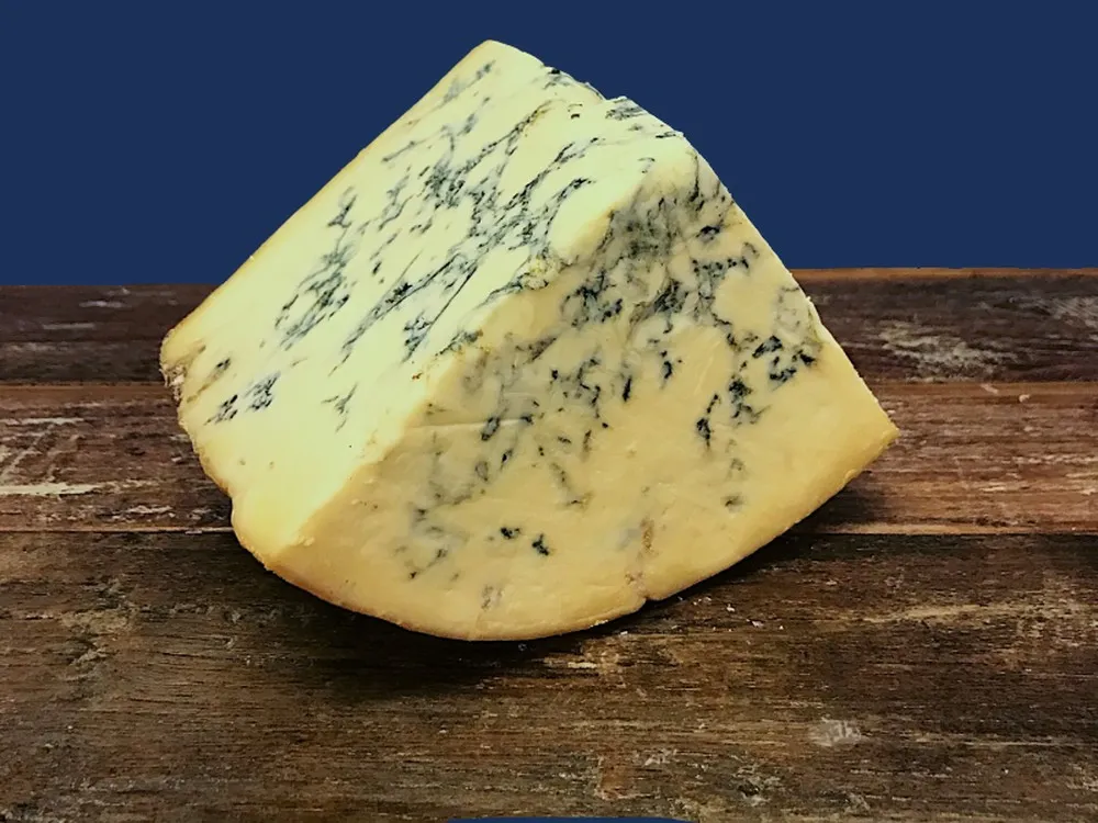 A wedge of Stichelton cheese showcasing its ivory interior streaked with blue veins