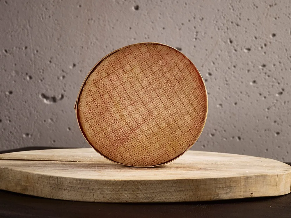 A round-shaped Stinking Bishop cheese with a brownish rind placed on a wooden surface