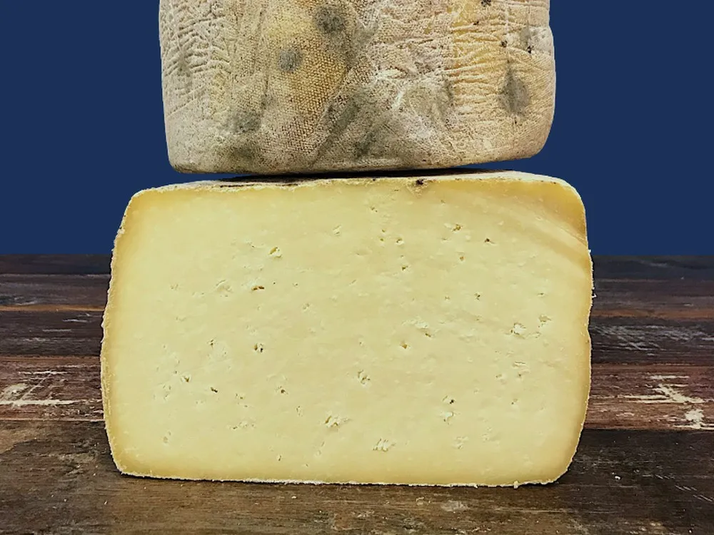 Slices of Swaledale cheese are stacked on a wooden surface, set against a dark blue background