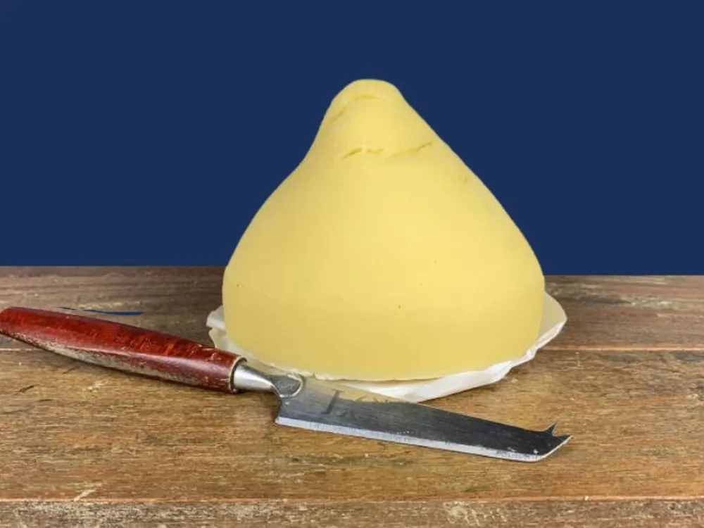 A pear-shaped, pale yellow Tetilla cheese, with a sharp knife nearby, rests on a wooden surface