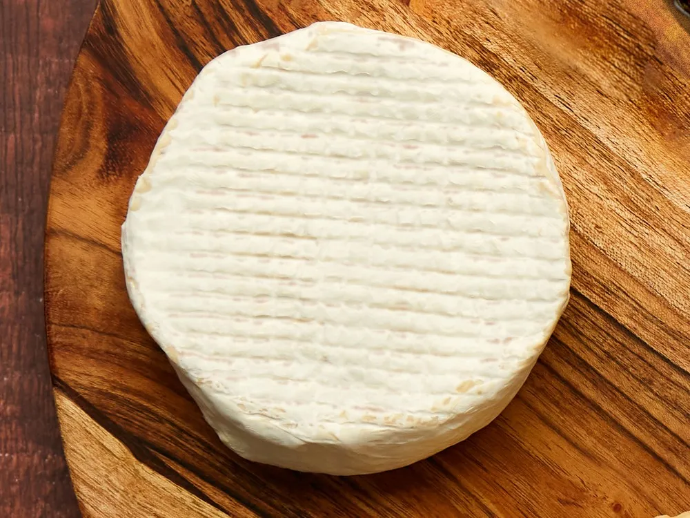 A disc of Truffle Camemvert, a plant-based Camembert alternative with a white bloomy rind, rests on a wooden surface