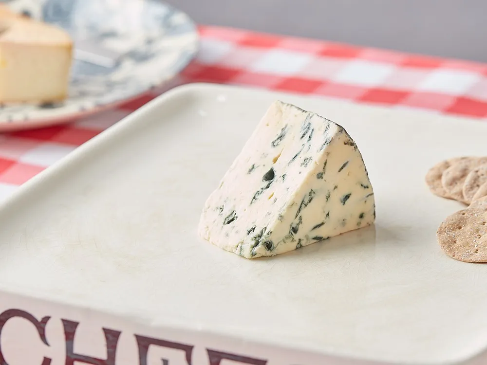 A slice of Yorkshire Blue cheese revealing blue veins on a pale yellow interior placed with crackers on a white plate