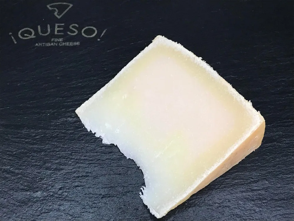 A slice of Zamorano cheese showing pale yellow interior placed on a black marble