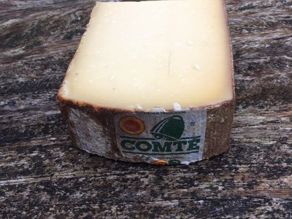 Aged Comte 30 months cheese with dark rind on a wooden surface