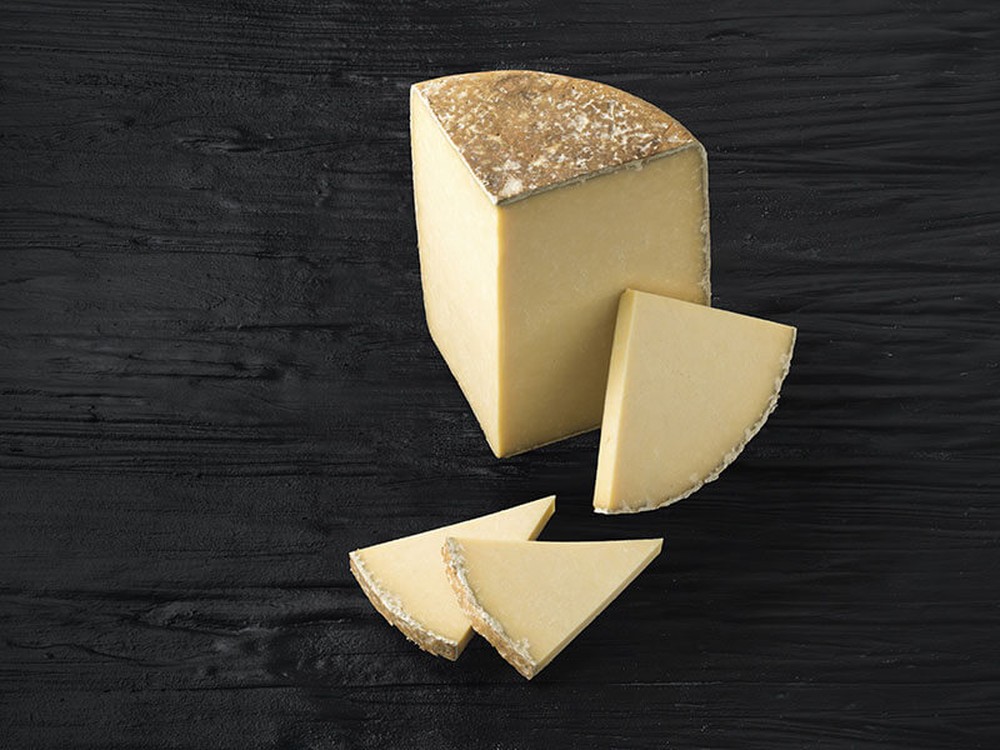 Slices of Cantal cheese revealing its pale yellow interiror and natural rind placed on a black wooden surface