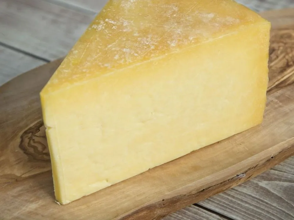 A triangular piece of Finlay's Cheddar cheese, highlighting its rich yellow interior, rests on a wooden surface