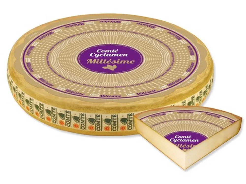 A wheel of Comté Cyclamen Millésime 24 Month cheese with a label, and a labeled triangular slice are displayed against a white background.